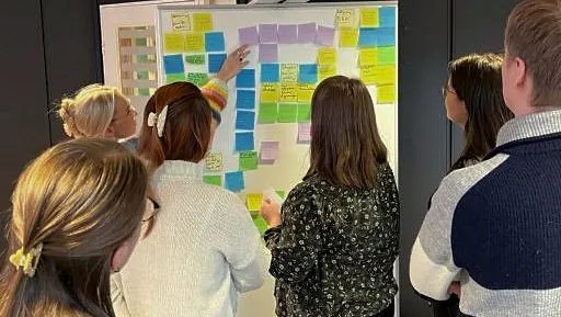 Traineer engasert i gruppearbeid med whiteboard og fargerike postit lapper